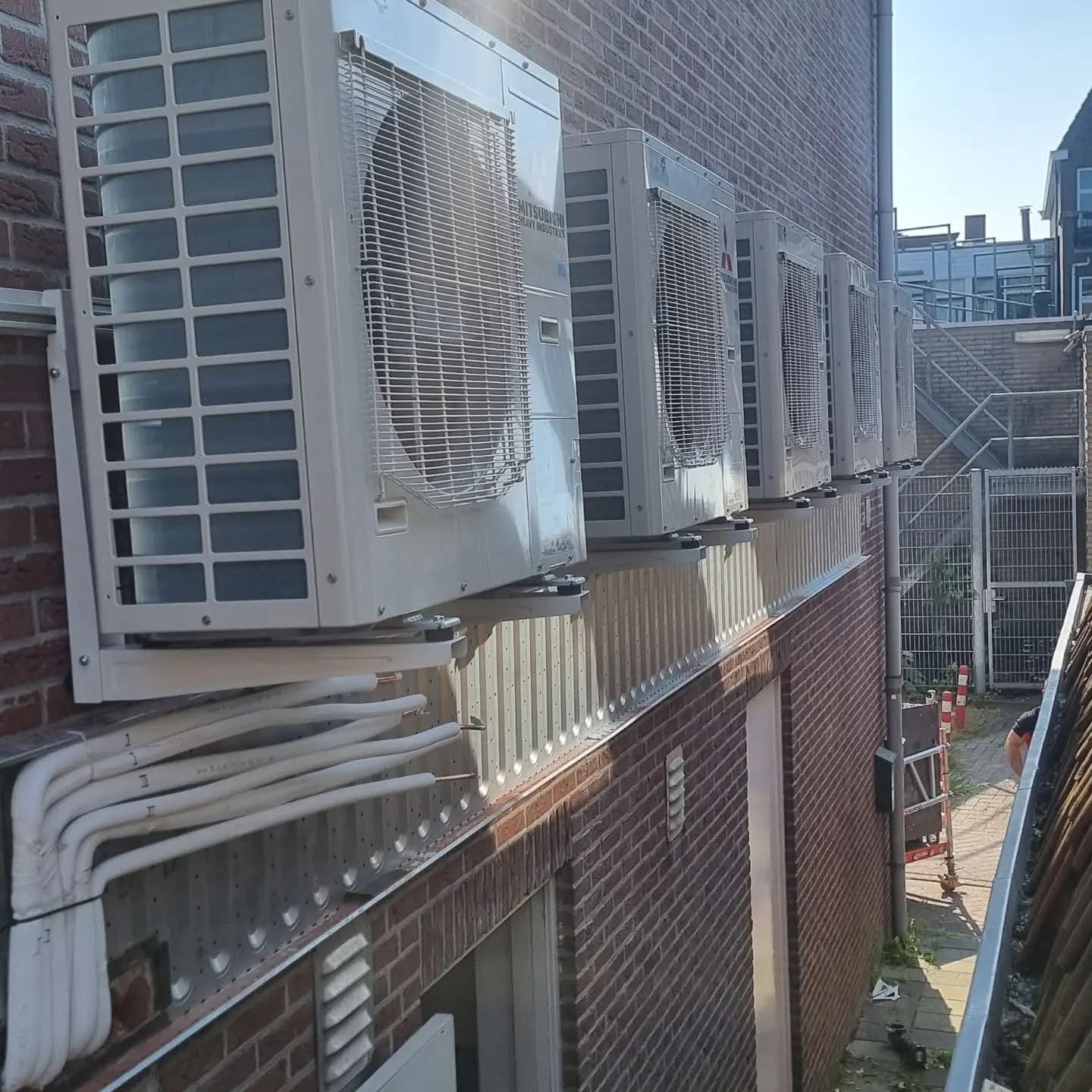Rij airco-buitenunits met weggewerkt leidingtracé bij een bedrijfspand